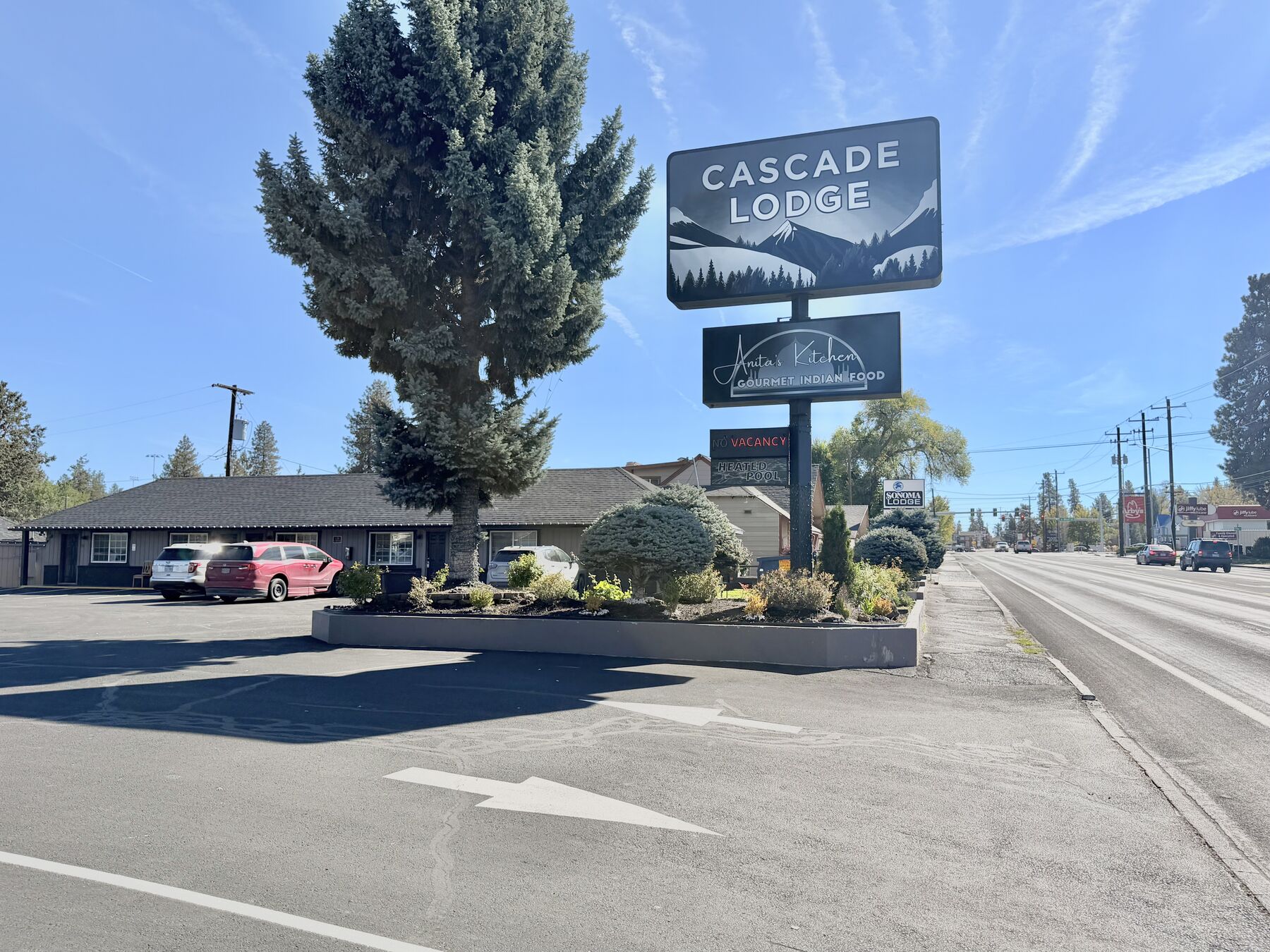 Cascade Lodge sign and single-story lodge building under a blue sky, with a tall evergreen and landscaped entry