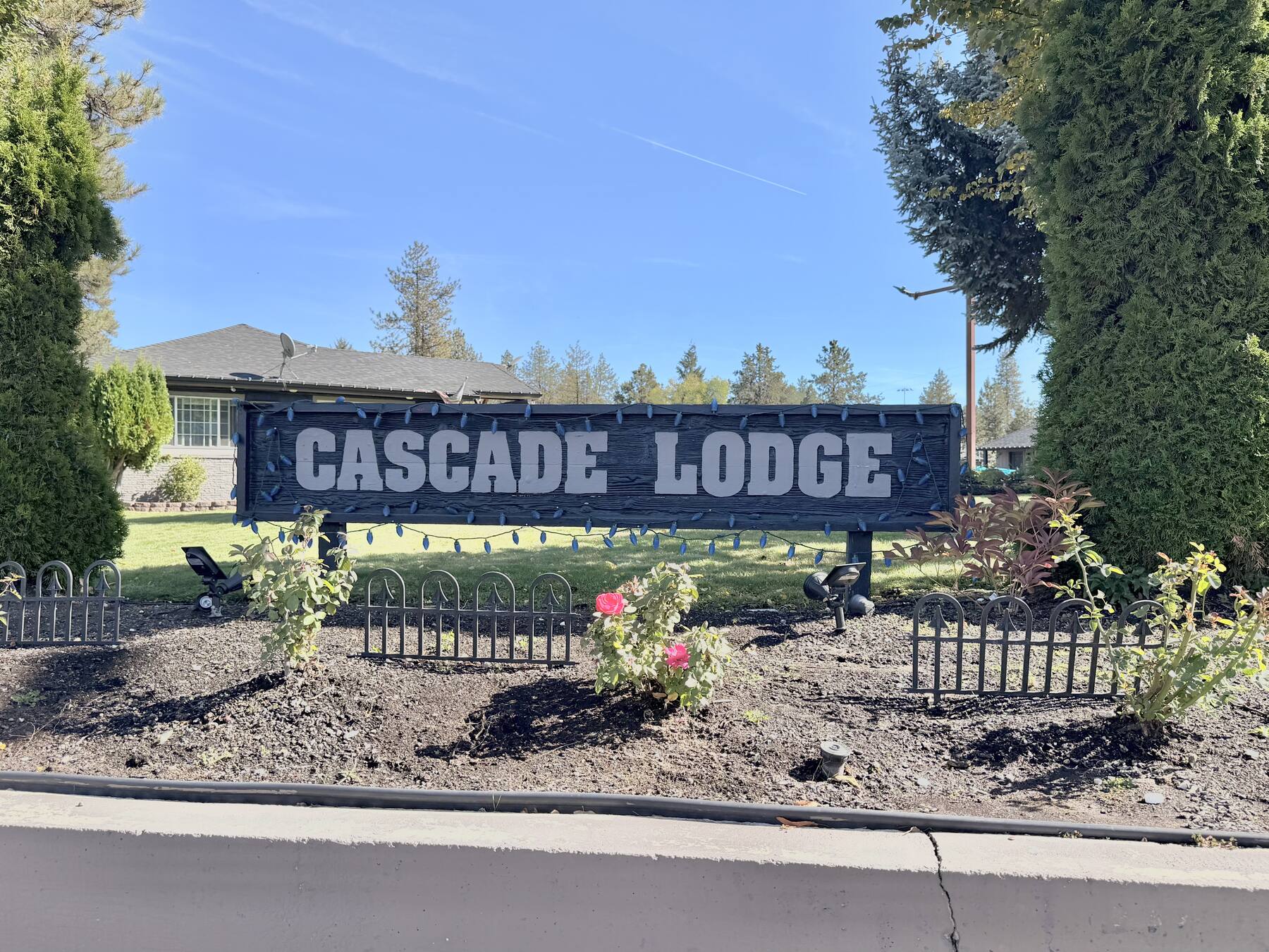 Cascade Lodge sign in a flower bed with evergreens and the lodge buildings behind it