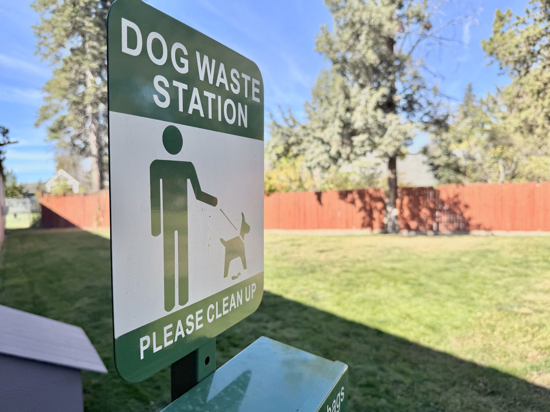 Dog waste station sign reading Please Clean Up beside the pet lawn
