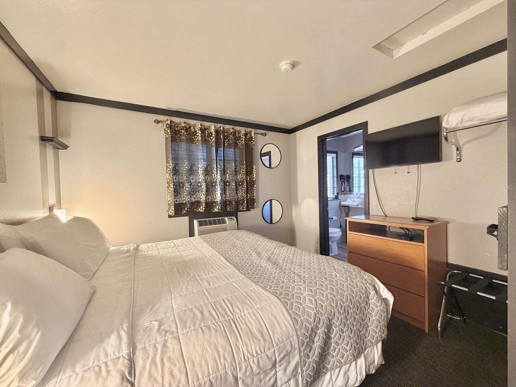 Broken Top King Spa Suite bedroom with a king bed, dresser with TV, luggage rack, and a doorway to the bathroom