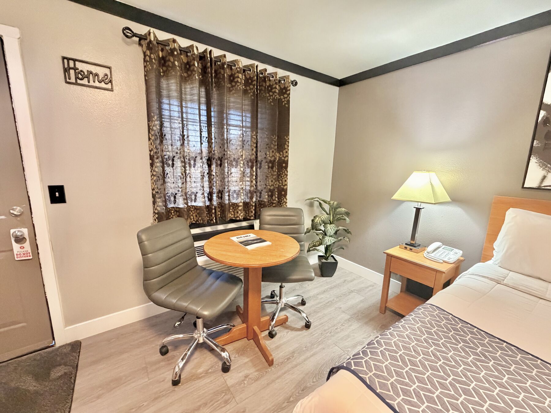 Cascade Queen sitting area with a round table and two chairs by the curtained window, next to the bedside lamp and phone