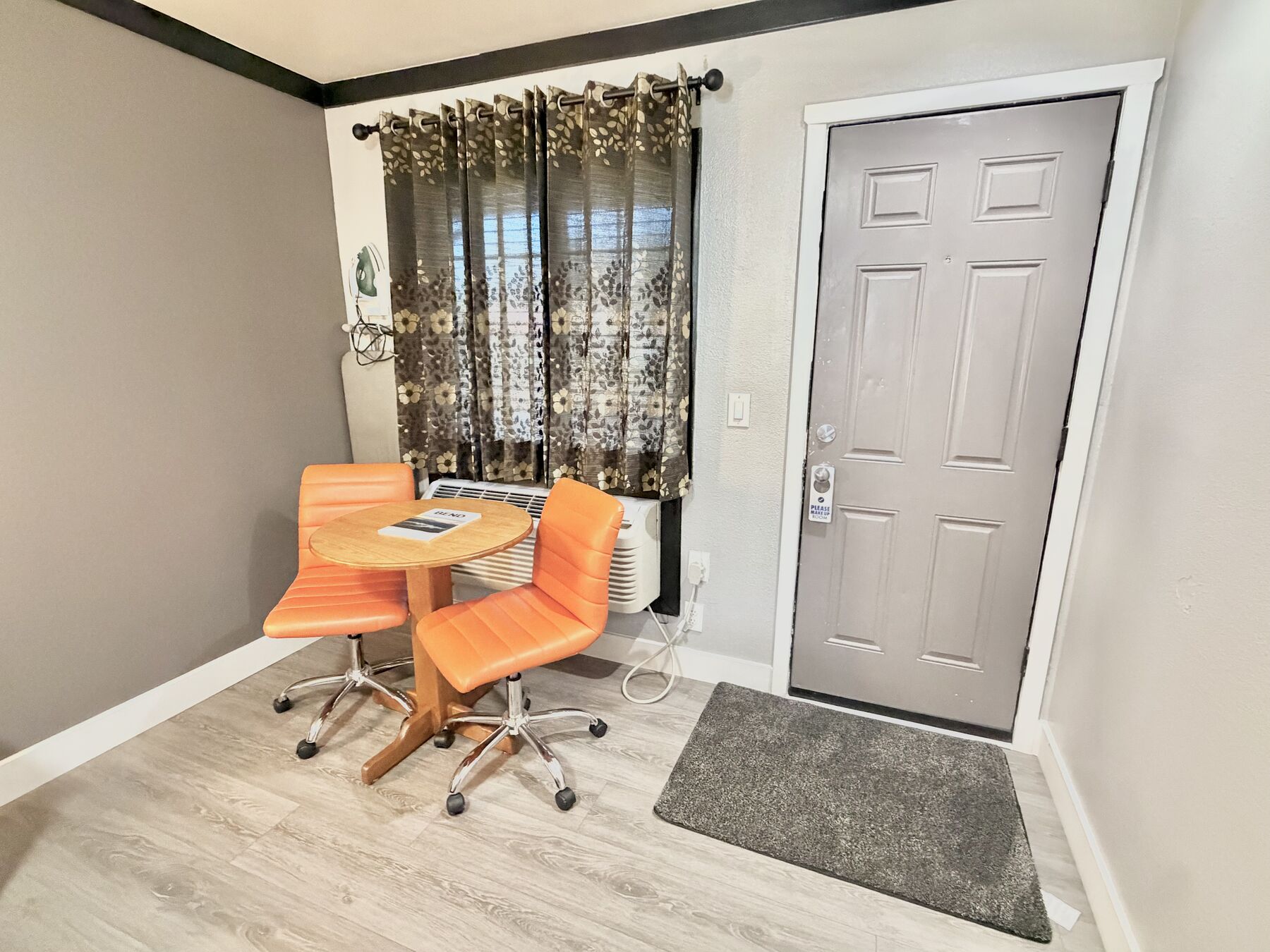 Cascade Queen sitting area with a round table and two orange chairs by the curtained window, next to the entry door