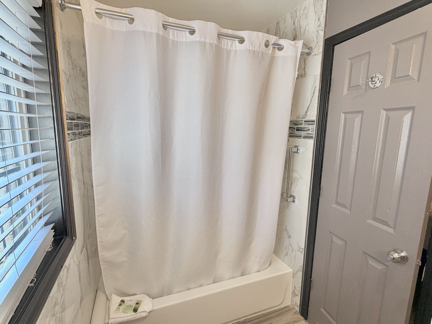 Cascade Queen bathroom tub and shower with marble-look tile, a white shower curtain, and a grab bar