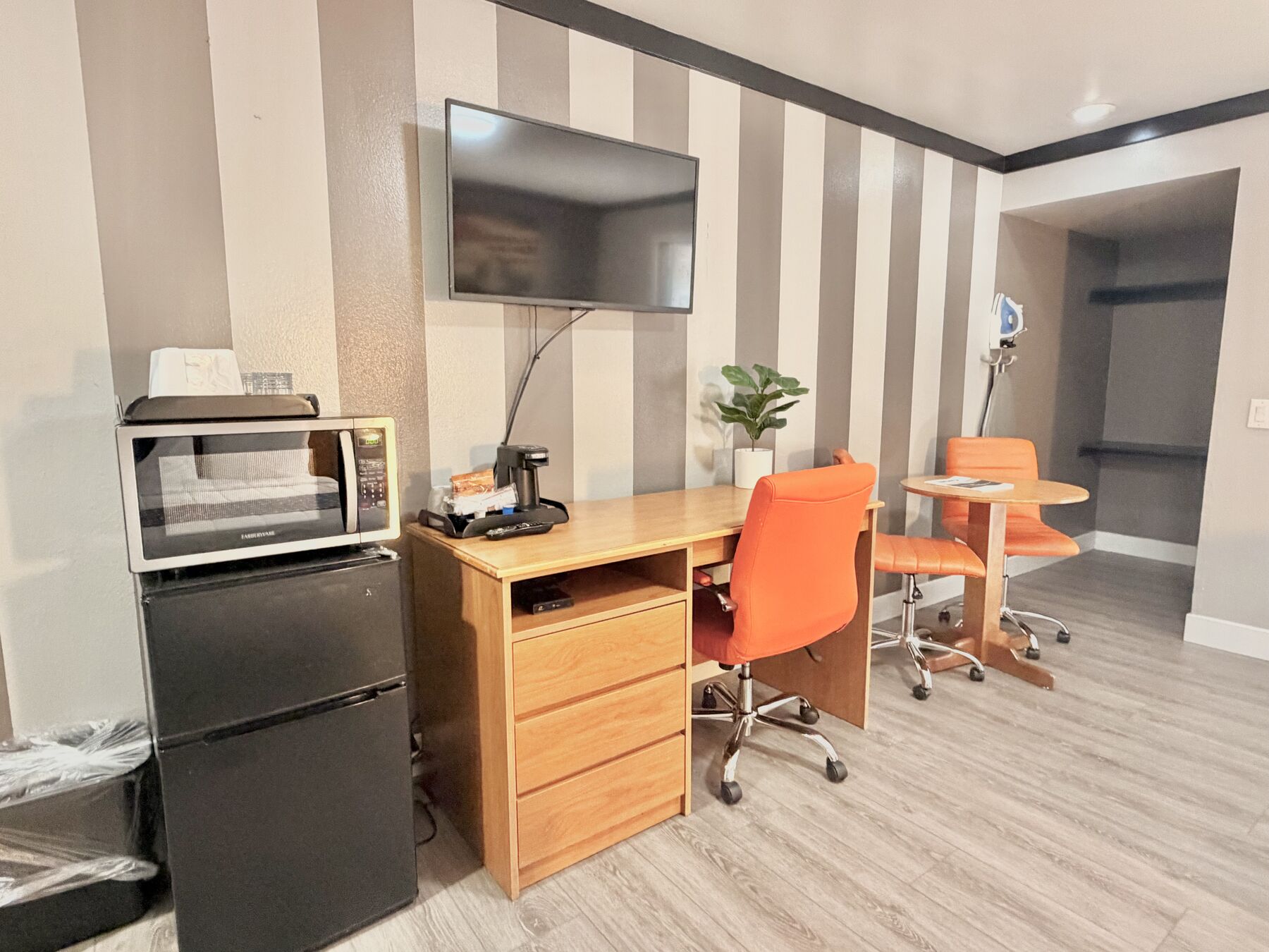 Deschutes Double Queen work desk with orange chair, wall-mounted TV, microwave, and mini fridge, with a small table by the closet