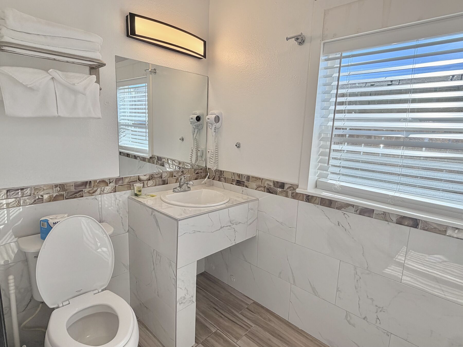 Deschutes Double Queen bathroom with marble-look tile, a pedestal sink, lit mirror, hair dryer, and towels