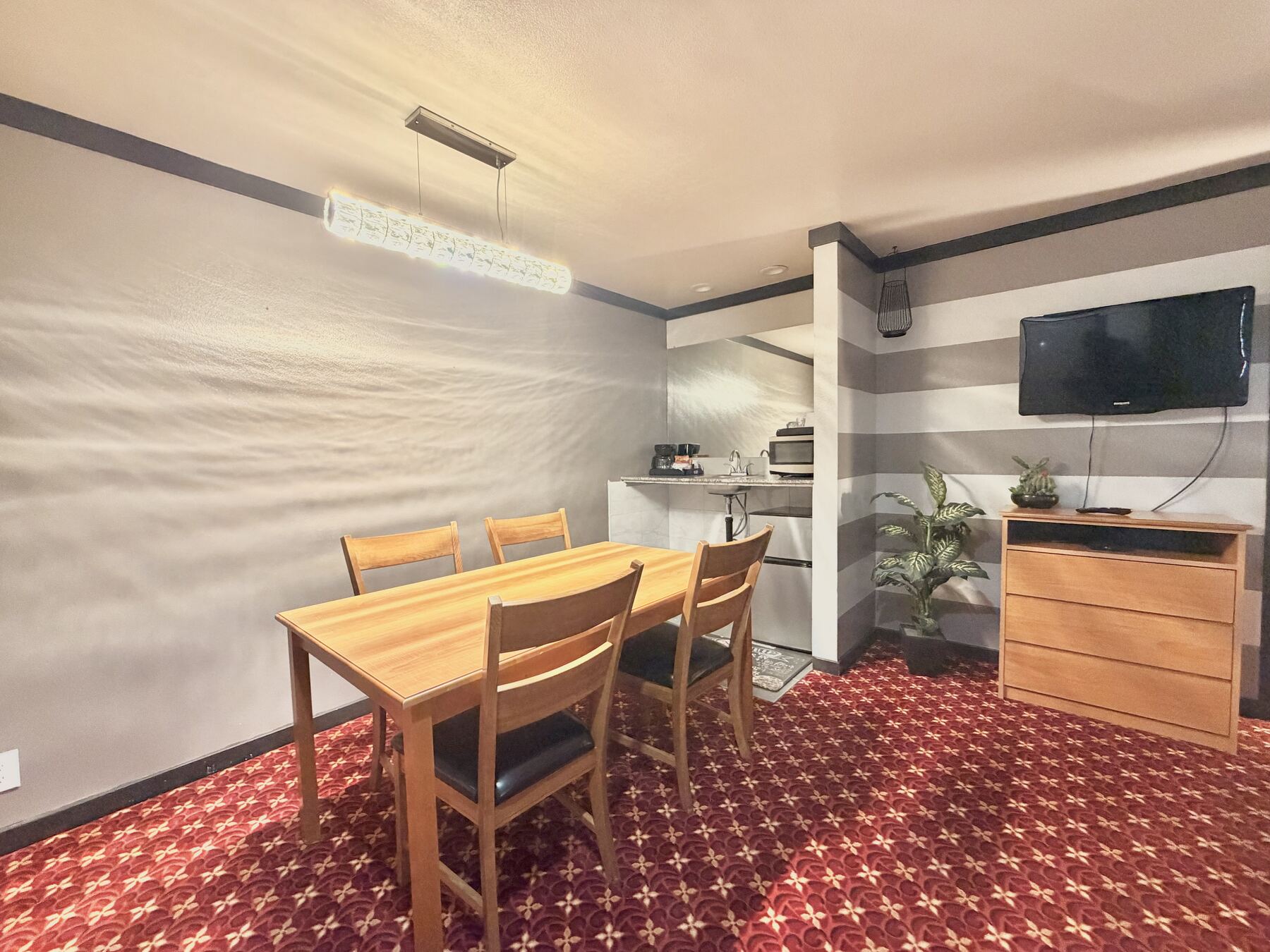 Sisters Queen Spa Suite dining table seating four under a pendant light, with the TV and kitchenette beyond